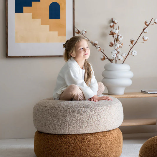 Runder Sitzsack Ottoman für Kinder von Wigiwama. Kind sitzt auf zwei übereinander gestapelten Sitzsäcken in der Farbe beige und Senf