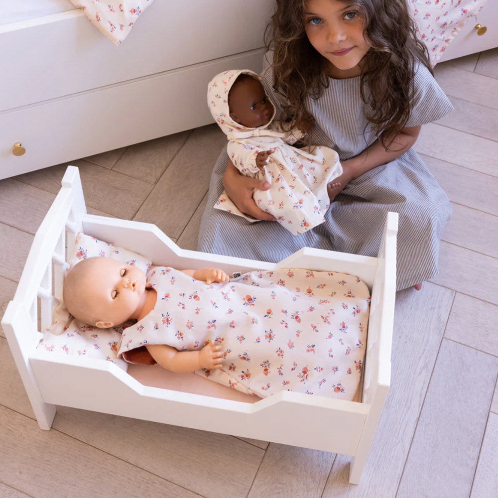 Mädchen sitzt vor dem Puppenbett und spielt mit zwei Puppen