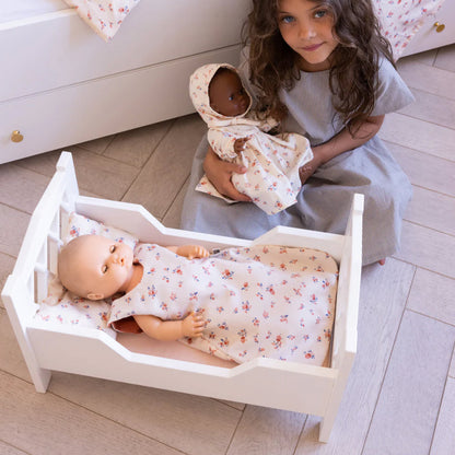 Mädchen sitzt vor dem Puppenbett und spielt mit zwei Puppen