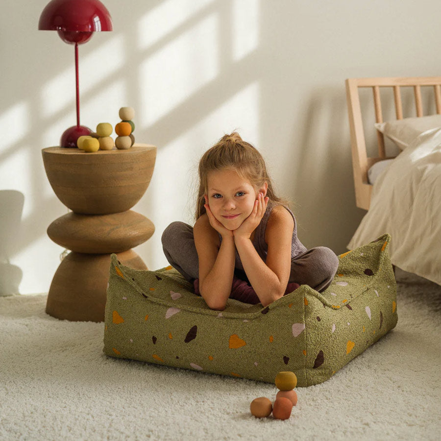 Schulkind sitzt auf dem Ottoman Sitzsack von Wigiwama in der Farbe Moos. Sehr stylisch